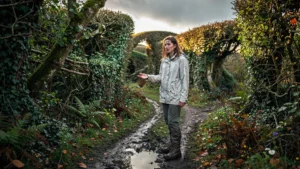 Femme perdue dans le bocage sans carte IGN, chemin boueux et haies denses sous lumière douce